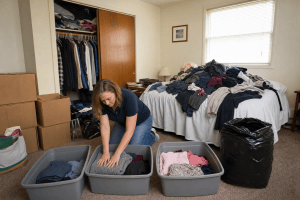 Clearview Cleaning and Organizing organizer sorting clothes into keep, donate and discard bins on the floor of a cluttered spare bedroom in an Englewood, Colorado home